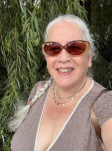 Victoria Klum shown wearing sunglasses and her white hair in a braid poses in front of a tree